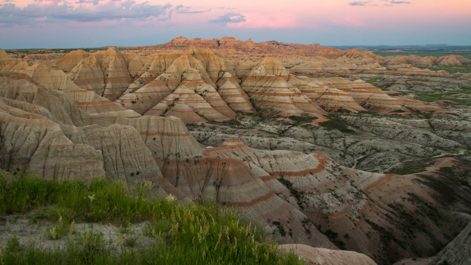 Layered rock formations beneath a pink evening sky in Badlands National Park